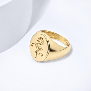 May include: A polished gold signet ring featuring an oval face with an engraved floral motif. The interior of the band is clearly stamped with the hallmark 585, indicating the gold purity of the piece. The ring has a smooth, reflective finish.