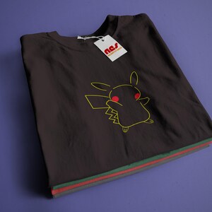 May include: A black t-shirt featuring a yellow outline of Pikachu with red eyes. The t-shirt is folded and has a white tag with the text "nss" on it.