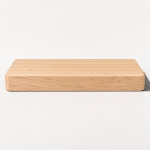 May include: A rectangular block of light-coloured natural wood with a smooth, flat top surface and visible grain patterns running horizontally across the front face. The object has rounded edges and a solid, uniform construction throughout.