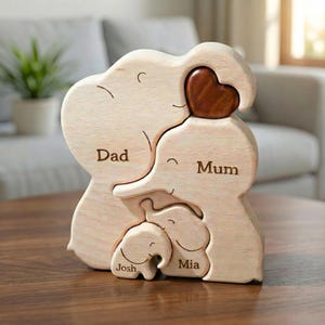 May include: A light-coloured wooden puzzle featuring four interlocking elephant figures. The largest elephant is labelled Dad, the second largest is labelled Mum, and the two smaller elephants are labelled Josh and Mia. A dark brown wooden heart sits at the top.