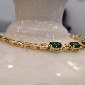 May include: A gold bracelet with a chain link design and oval-shaped green gemstones. The bracelet has small clear stones set in the metal between the green stones.