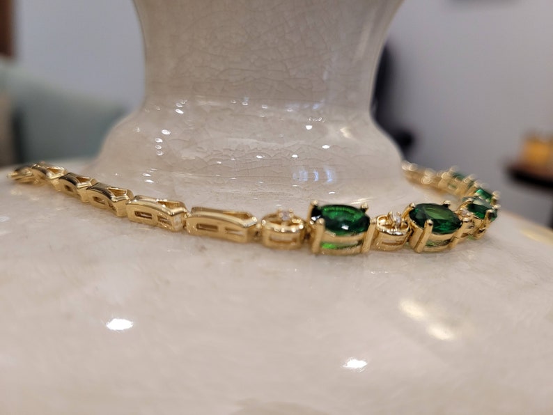 May include: A gold bracelet with a chain link design and oval-shaped green gemstones. The bracelet has small clear stones set in the metal between the green stones.