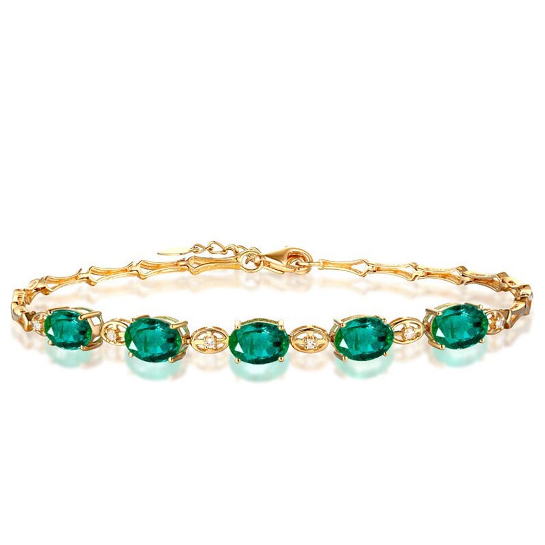 May include: A gold bracelet with a delicate chain and five oval-shaped green gemstones. The gemstones are surrounded by smaller, clear gemstones.