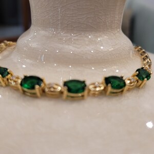 May include: A gold bracelet with emerald green gemstones. The bracelet has a delicate design with small, clear stones between the larger green stones.