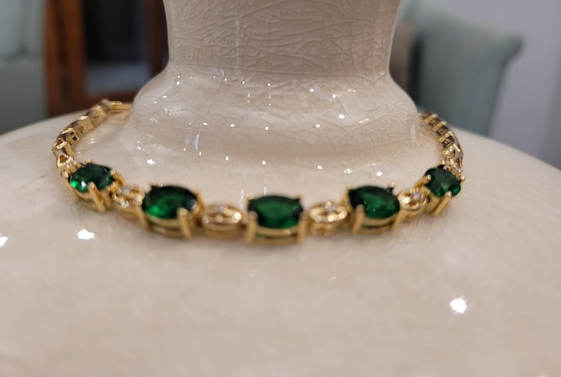 May include: A gold bracelet with emerald green gemstones. The bracelet has a delicate design with small, clear stones between the larger green stones.