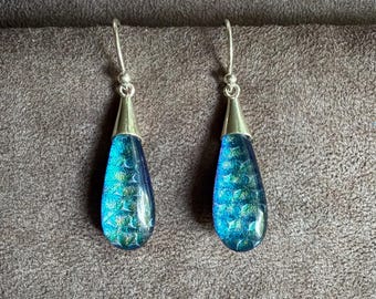 May include: A pair of drop earrings featuring teardrop-shaped pendants with a vibrant blue and green iridescent scale pattern. The pendants are suspended from silver-toned metal hooks, creating a sleek and reflective appearance for these jewelry pieces.