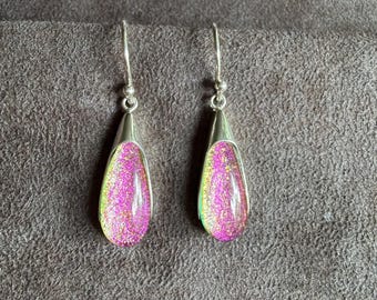 May include: A pair of drop earrings featuring teardrop-shaped glass cabochons with a vibrant pink and gold iridescent finish. The glass pieces are set in polished silver-tone metal caps and hang from matching silver-tone curved ear wires.
