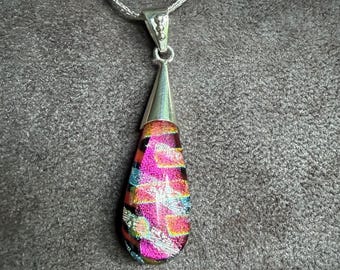 May include: A teardrop-shaped dichroic glass pendant featuring vibrant pink, orange, and teal geometric patterns. The glass is set in a polished silver-toned metal cap and hangs from a matching silver-toned chain necklace.