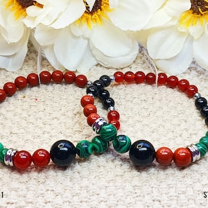Puede incluir: Dos pulseras con cuentas negras, rojas y verdes. Las pulseras están etiquetadas como "Style 1" y "Style 2".