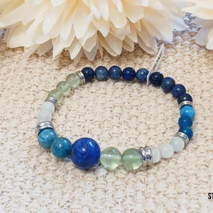 Pode incluir: Um bracelete de contas azuis, verdes e brancas com espa&ccedil;adores prateados. O bracelete apresenta uma grande pedra preciosa azul no centro.