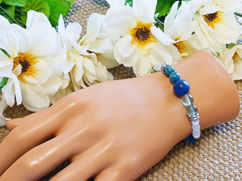 Pode incluir: Um bracelete com contas azuis, verdes e brancas sobre um fundo branco. O bracelete &eacute; feito de pedras naturais e &eacute; enfiado em uma corrente de prata.