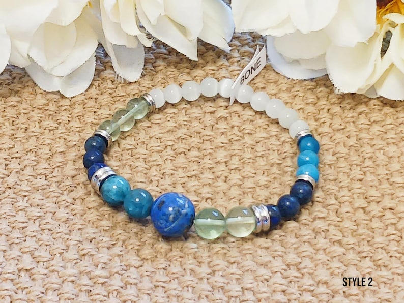 Pode incluir: Um bracelete de contas azuis, verdes e brancas com detalhes prateados. O bracelete tem uma conta azul grande no centro. O texto "BONE" &eacute; vis&iacute;vel em uma etiqueta branca.