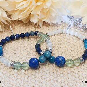 Pode incluir: Duas pulseiras de contas com pedras azuis, verdes e brancas. A pulseira da esquerda tem um fecho prateado e a pulseira da direita tem um fecho de pedra branca. As pulseiras s&atilde;o etiquetadas como "STYLE 1" e "STYLE 2".