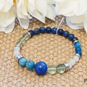 Pode incluir: Um bracelete de contas azuis, verdes e brancas com espa&ccedil;adores prateados. O bracelete tem uma grande pedra preciosa azul no centro.