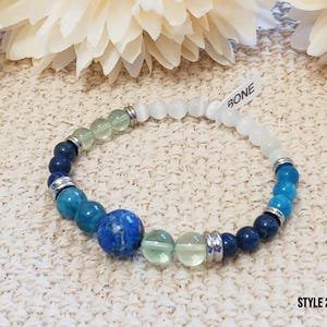 Pode incluir: Um bracelete de contas azuis, verdes e brancas com um fecho de prata. O bracelete tem uma etiqueta que diz "BONE" e "STYLE 2".