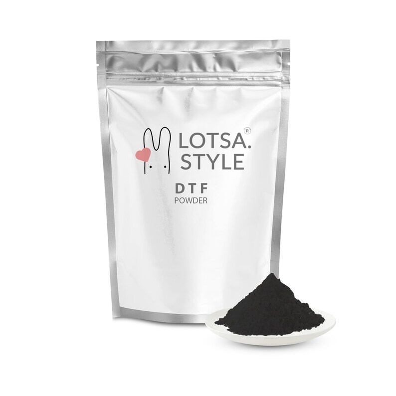 May include: A silver pouch with a white label that reads "LOTSA. STYLE DTF POWDER". A small pink heart is next to the bunny logo. A small white dish with a pile of black powder sits in front of the pouch.