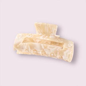 May include: A large, off-white hair claw with a marbled pattern. The claw is made of plastic and has a smooth, glossy finish.
