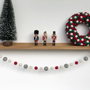 Op de afbeelding: Een houten plank met een guirlande van rode en groene viltballen, een kleine kunstkerstboom en drie notenkrakerfiguren.