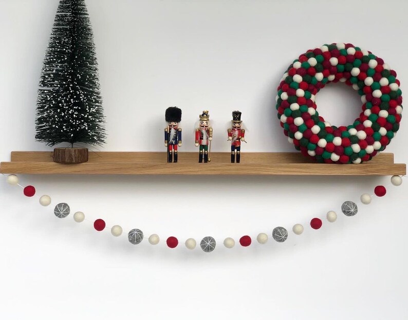 Op de afbeelding: Een houten plank met een guirlande van rode en groene viltballen, een kleine kunstkerstboom en drie notenkrakerfiguren.