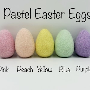 May include: Five pastel felt Easter eggs in a row. From left to right, the colours are pink, peach, yellow, blue, and purple. The eggs are labelled with their colours below them.