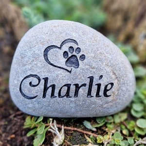 Op de afbeelding: Een grijze steen gegraveerd met een hart en een pootprint, en de naam "Charlie".