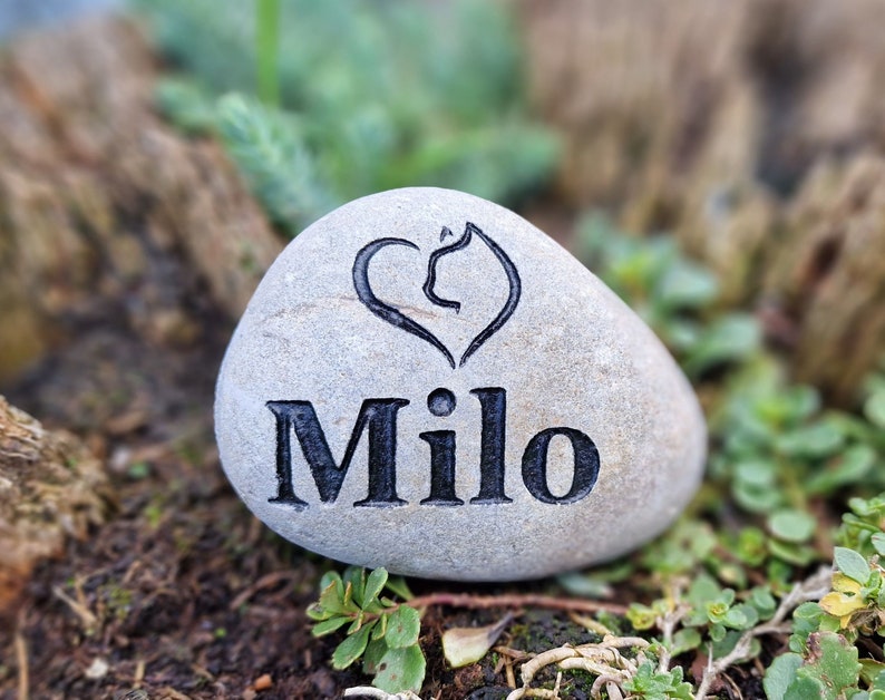 Op de afbeelding: Een grijs stenen hart gegraveerd met een pootprint en de naam "Milo".