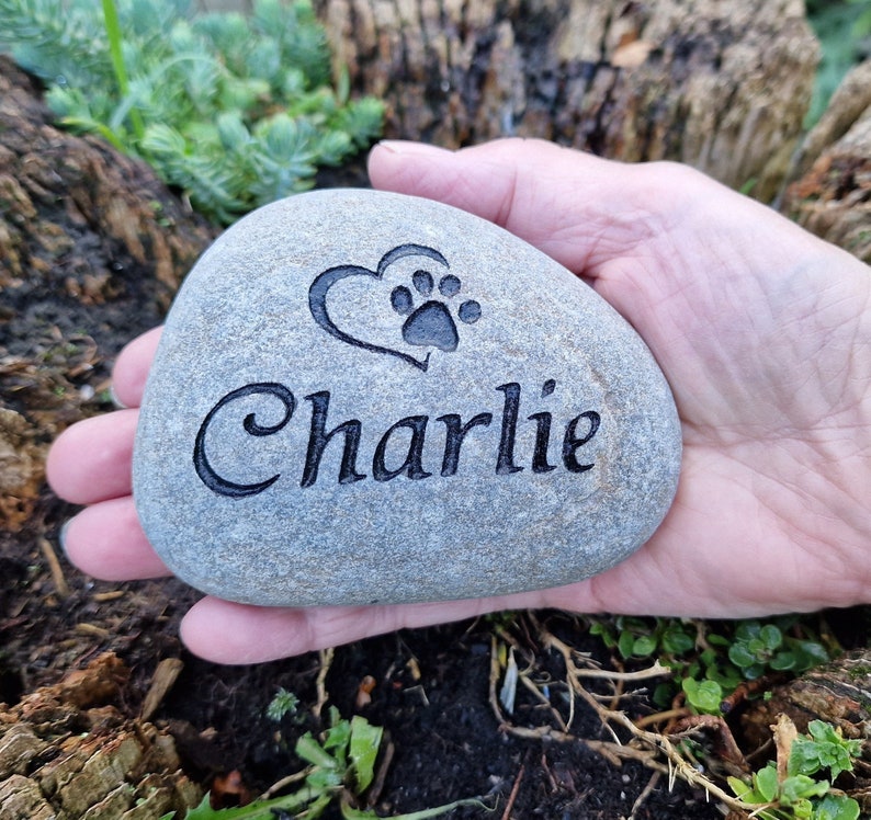 Op de afbeelding: Een grijze steen gegraveerd met een pootprint in een hart en de naam "Charlie".