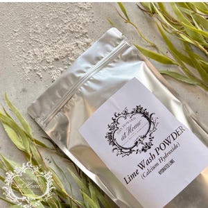 May include: A silver metallic resealable pouch containing Lime Wash Powder, also labeled as Calcium Hydroxide and Hydrated Lime. The white label features the text Amy Howard at Home in a decorative black frame, with loose white powder nearby.