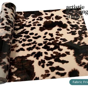 May include: A roll of transfer foil featuring a brown and black cow print pattern on a cream background. The text artistic painting studio is printed in the upper right corner, and a teal label reads Fabric Friendly in the bottom right corner.
