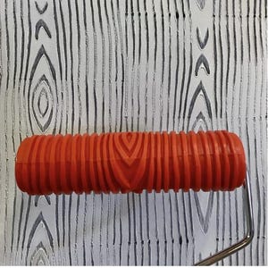 May include: An orange paint roller with a wood grain pattern is positioned over a surface with a matching wood grain design. The roller's handle is silver. The background features vertical lines and wood grain details.
