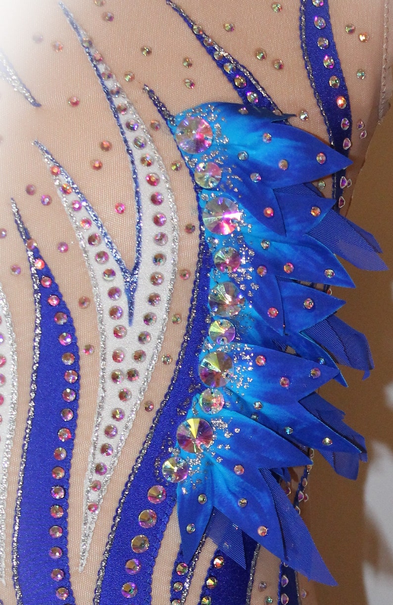 May include: A close-up of a blue and white leotard with rhinestones. The leotard has a blue and white striped pattern and a blue and turquoise flower design on the right shoulder.