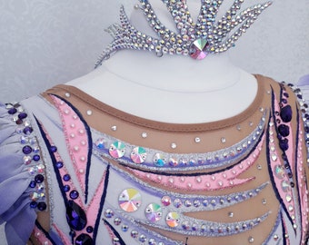 May include: A rhythmic gymnastics leotard featuring a nude mesh bodice with intricate white, pink, and purple fabric overlays, heavily embellished with iridescent crystals and dark purple stones, paired with a matching crystal-encrusted crown headpiece.