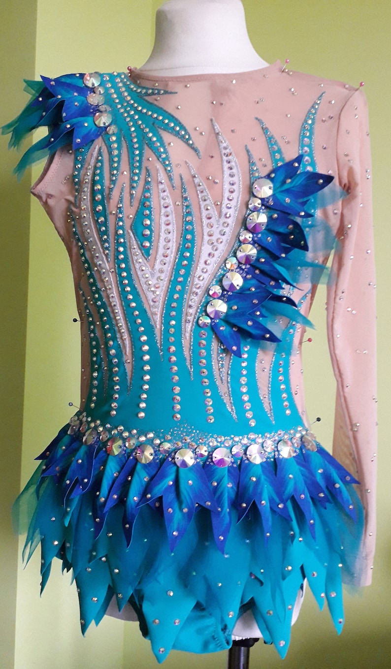 May include: A turquoise and blue leotard with a long sleeve design. The leotard is decorated with rhinestones and feathers. The leotard has a skirt with a scalloped edge.