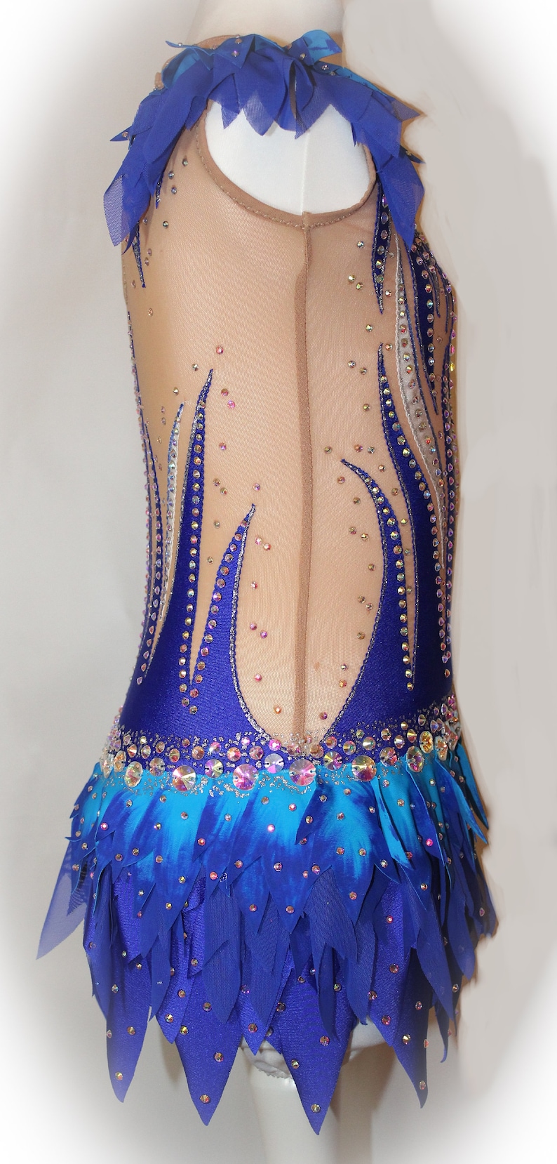 May include: A blue and turquoise leotard with a layered skirt and rhinestones. The leotard has a sheer bodice and a blue and white design.