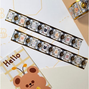Könnte beinhalten: Dekoratives Washi-Tape mit Spielkartenmotiven und Tierillustrationen, darunter Kaninchen, Katzen und Bären. Das Tape hat goldene Akzente und wird mit einer "Hello"-Karte mit einem Bären mit Fliege präsentiert.