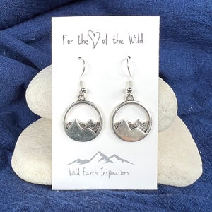 May include: Silver earrings with a mountain range design inside a circle. The earrings are on a white card with the text "For the ♥ of the Wild" and "Wild Earth Inspirations".
