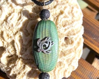 May include: A green and black wood pendant necklace with a silver turtle charm. The necklace is made with black lava beads and a green and black wood pendant.