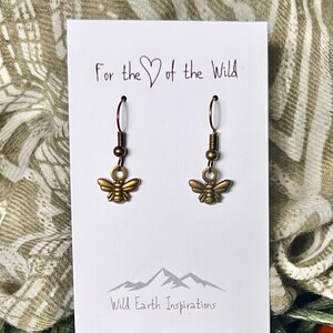 May include: A pair of gold-toned bee earrings on a white card with the text "For the ♥ of the Wild" and "Wild Earth Inspirations".