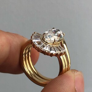 Puede incluir: Un anillo de oro con un gran diamante de forma ovalada engastado en un halo en forma de abanico de diamantes m&aacute;s peque&ntilde;os. El anillo est&aacute; montado sobre una banda con tres filas de oro.