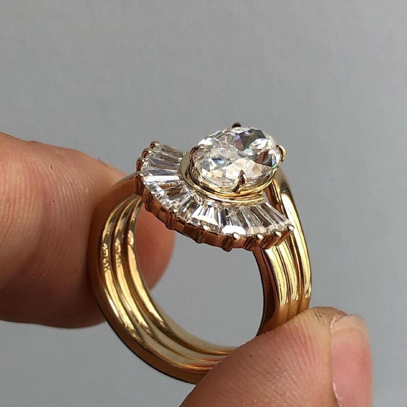 Puede incluir: Un anillo de oro con un gran diamante de forma ovalada engastado en un halo en forma de abanico de diamantes m&aacute;s peque&ntilde;os. El anillo est&aacute; montado sobre una banda con tres filas de oro.