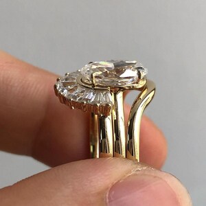 Puede incluir: Un anillo de oro con un gran diamante de forma ovalada engastado en un halo de diamantes m&aacute;s peque&ntilde;os. El anillo est&aacute; montado sobre una banda con un dise&ntilde;o delicado y curvado.