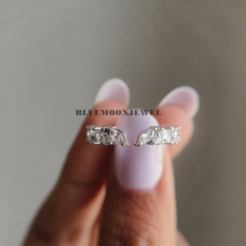 May include: A pair of silver rings with marquise-shaped clear stones set in a delicate, curved design.  The rings are open and can be worn on any finger.