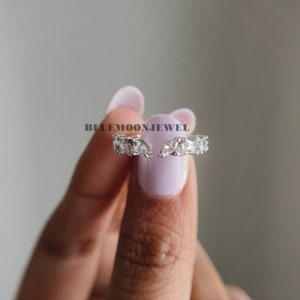 May include: A silver ring with a row of clear, round stones set in a curved shape. The ring is open and has a delicate design.