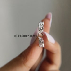 May include: A silver ring with a row of marquise-shaped clear stones. The ring is on a finger.