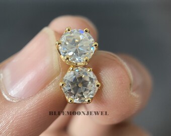 May include: A pair of gold stud earrings with round, clear gemstones. The earrings are held in a hand.