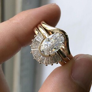 Puede incluir: Un anillo de oro con un gran diamante de forma ovalada rodeado de diamantes m&aacute;s peque&ntilde;os en forma de abanico.