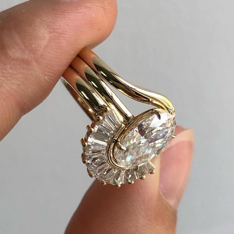 Puede incluir: Un anillo de oro con un gran diamante de forma ovalada rodeado por un halo de diamantes m&aacute;s peque&ntilde;os. El anillo est&aacute; montado en una banda con un dise&ntilde;o delicado y curvo.