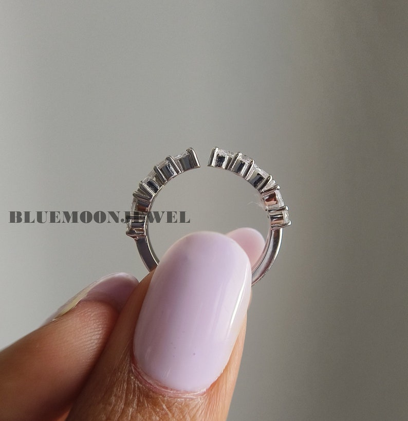 May include: A silver ring with a row of small, clear stones set in a half-circle shape. The ring is open on one side, allowing it to be adjusted to fit different finger sizes.