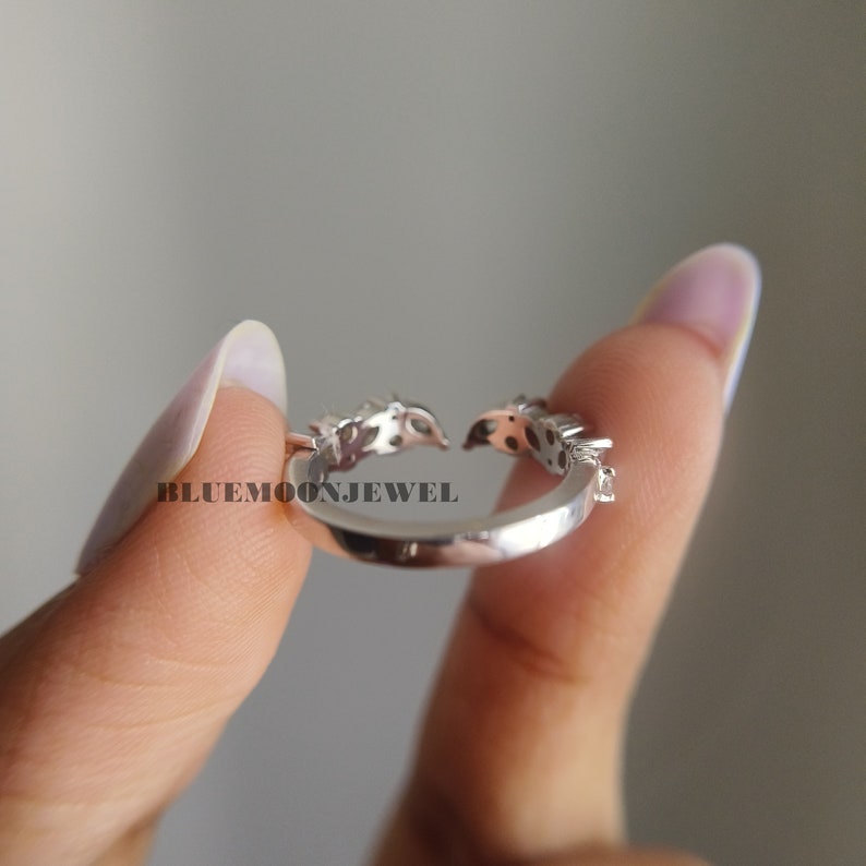 May include: A silver ring with a delicate design featuring small clear stones. The ring is open and adjustable.