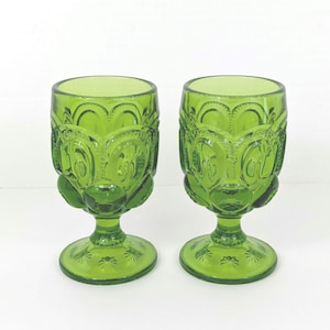 May include: A handmade wooden sign with the text "Welcome" in a whimsical font. The sign is painted white with a distressed finish, and features a decorative floral design in shades of pink and green. It measures approximately 12 inches wide.